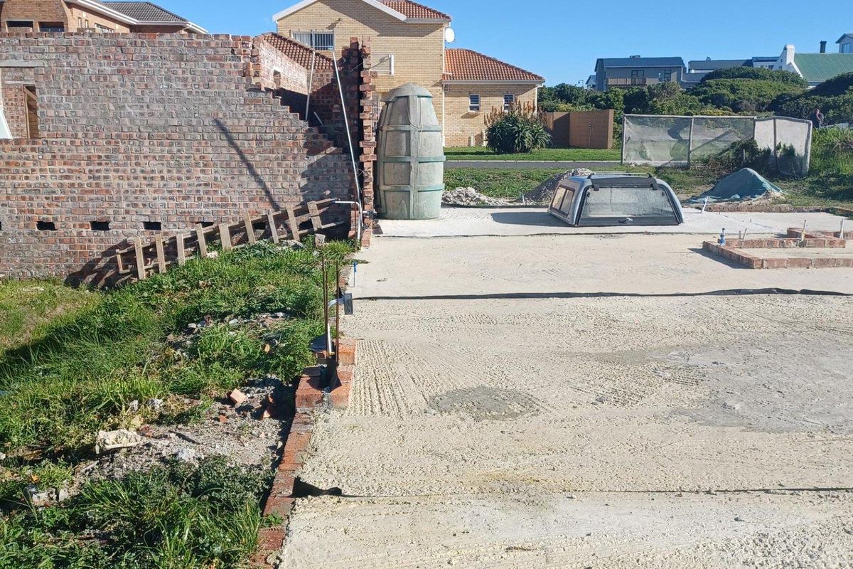 A view of a residential plot under construction, featuring a concrete slab foundation, partial brick walling, and an installed septic tank.