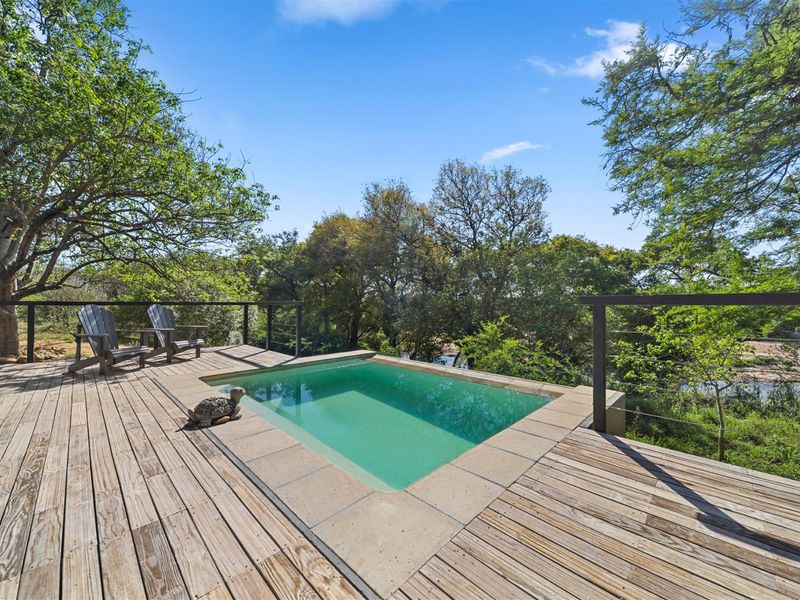A serene outdoor plunge pool set within a timber deck, featuring a metal safety railing and surrounded by lush natural vegetation.