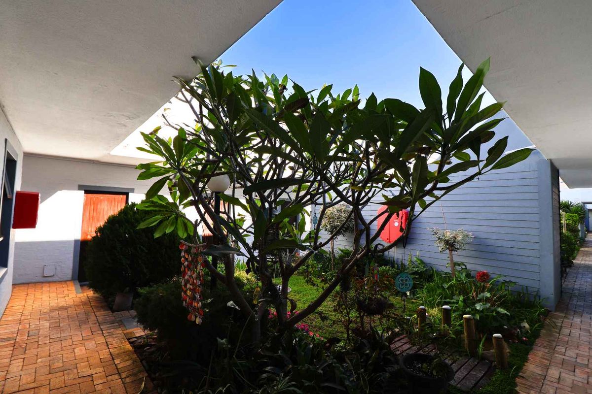 A well-maintained central courtyard area featuring brick paving, established garden beds, and a covered walkway providing access to the apartment units.