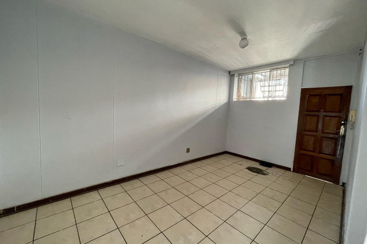An empty bedroom featuring tiled flooring, a wooden door, and a high-set window with security bars.