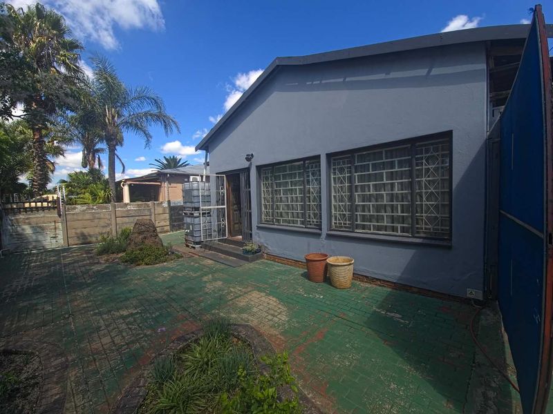Rear exterior view of the property featuring a paved courtyard area, security bars on windows, and a precast concrete boundary wall.