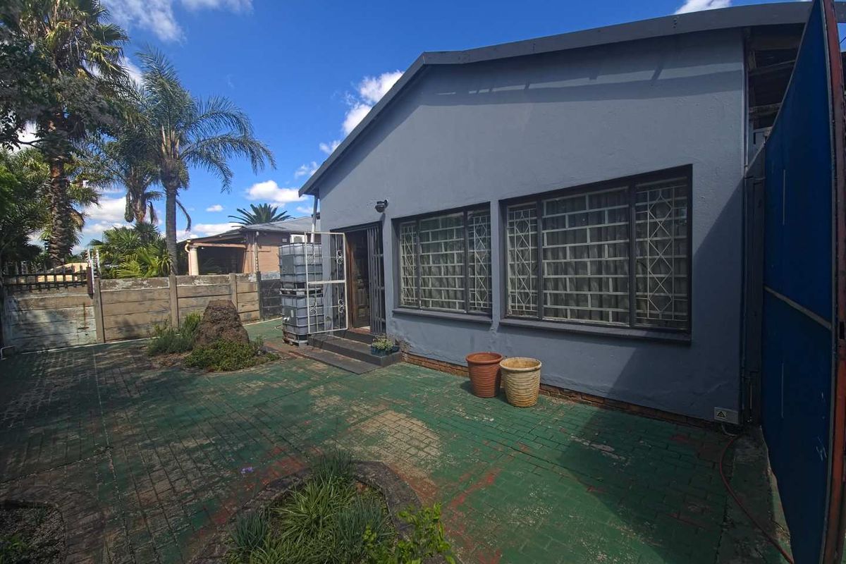Rear exterior view of the property featuring a paved courtyard area, security bars on windows, and a precast concrete boundary wall.