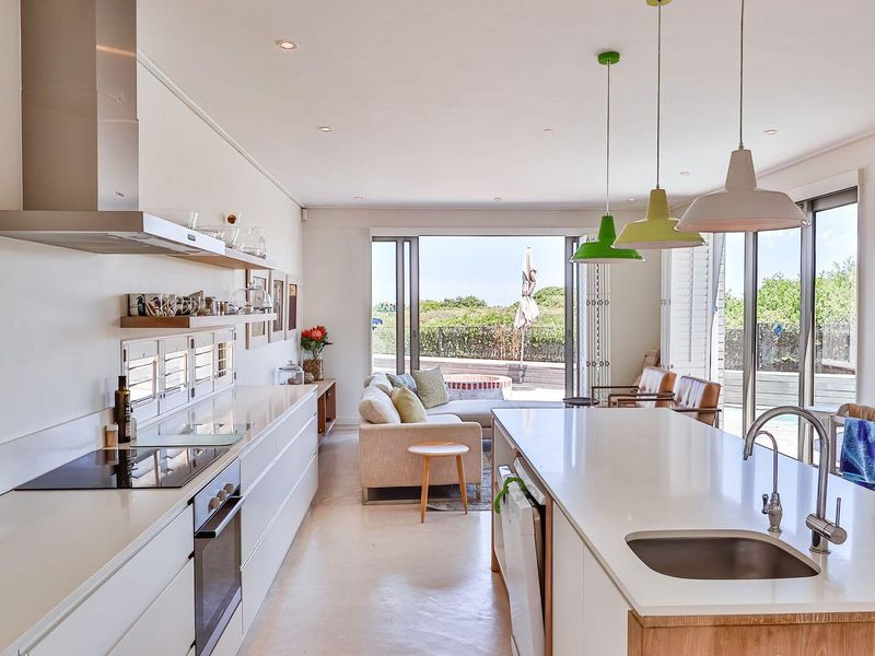 Modern open-plan kitchen and living area featuring sleek cabinetry, stone countertops, integrated appliances, and large sliding doors opening to an outdoor patio.