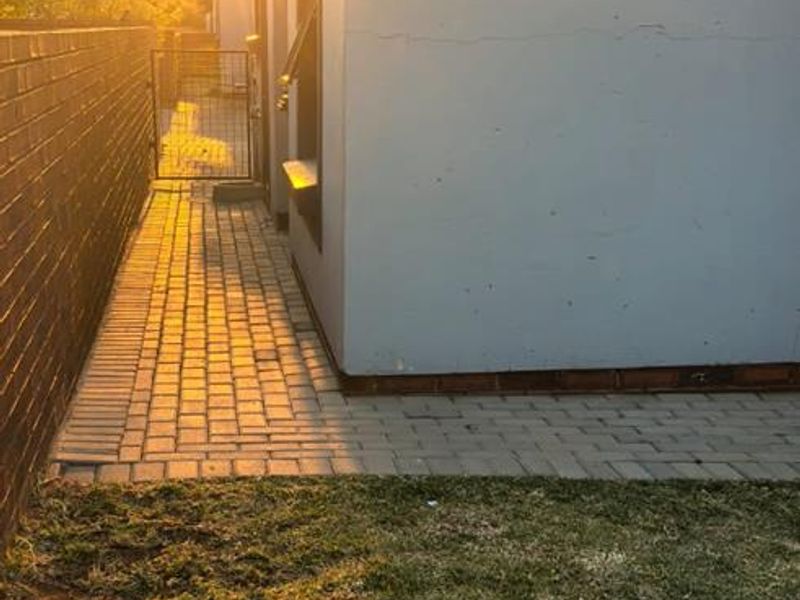 A side view of the property featuring a paved walkway, brick boundary wall, and a small lawn area at sunset.