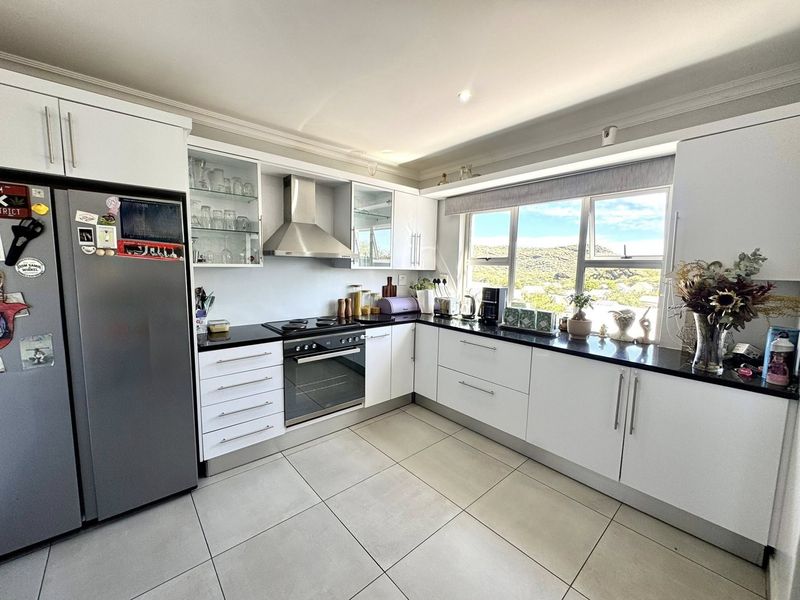 Modern kitchen featuring white cabinetry, black granite countertops, stainless steel appliances, and large windows with scenic views.