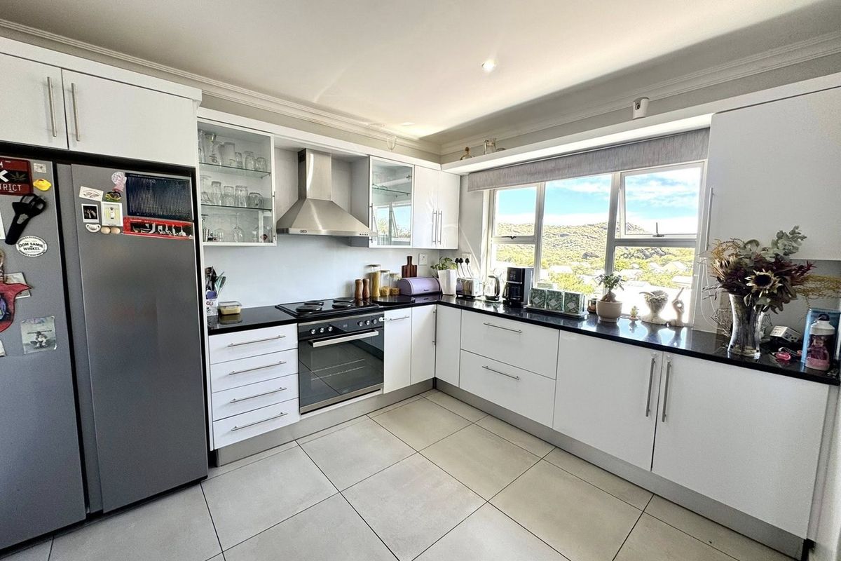 Modern kitchen featuring white cabinetry, black granite countertops, stainless steel appliances, and large windows with scenic views.