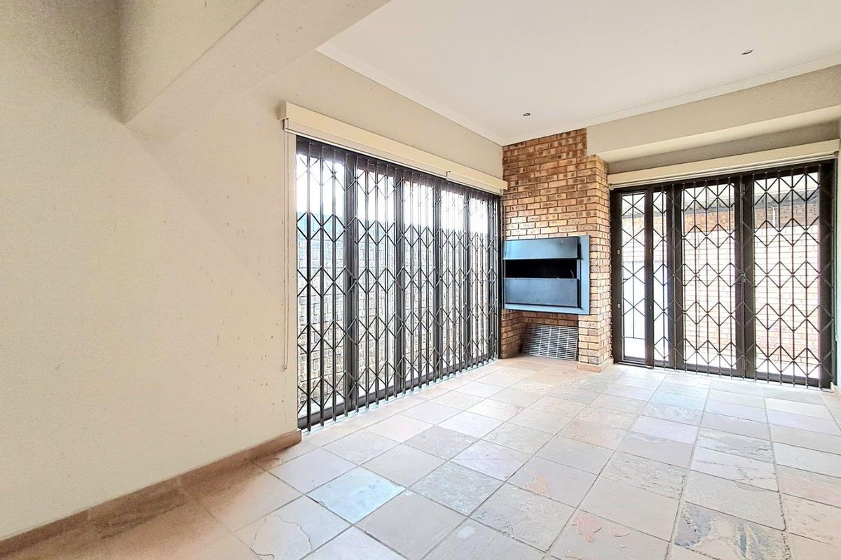 Spacious living area featuring a built-in brick fireplace, tiled flooring, and large sliding doors with security gates leading to the exterior.