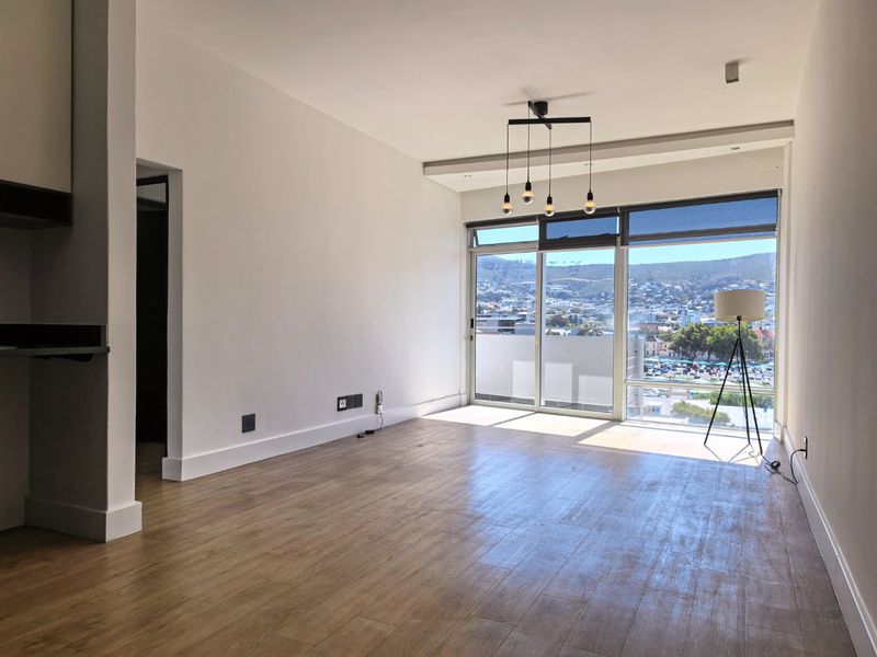A bright, open-plan living area featuring wood-look tile flooring, modern pendant lighting, and large sliding glass doors offering expansive city and mountain views.