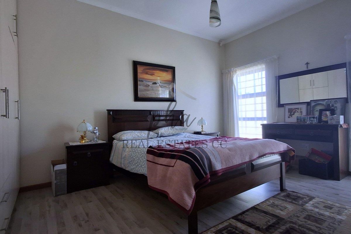 A well-maintained bedroom featuring built-in cupboards, laminate flooring, and natural light through a window with security bars.