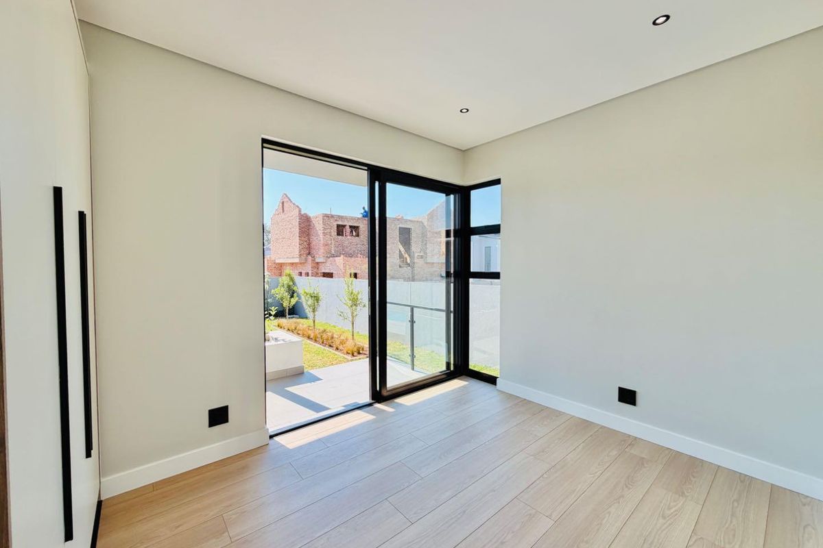 Modern, bright bedroom featuring light wood-look laminate flooring, built-in cupboards, and large sliding glass doors opening to an outdoor area.