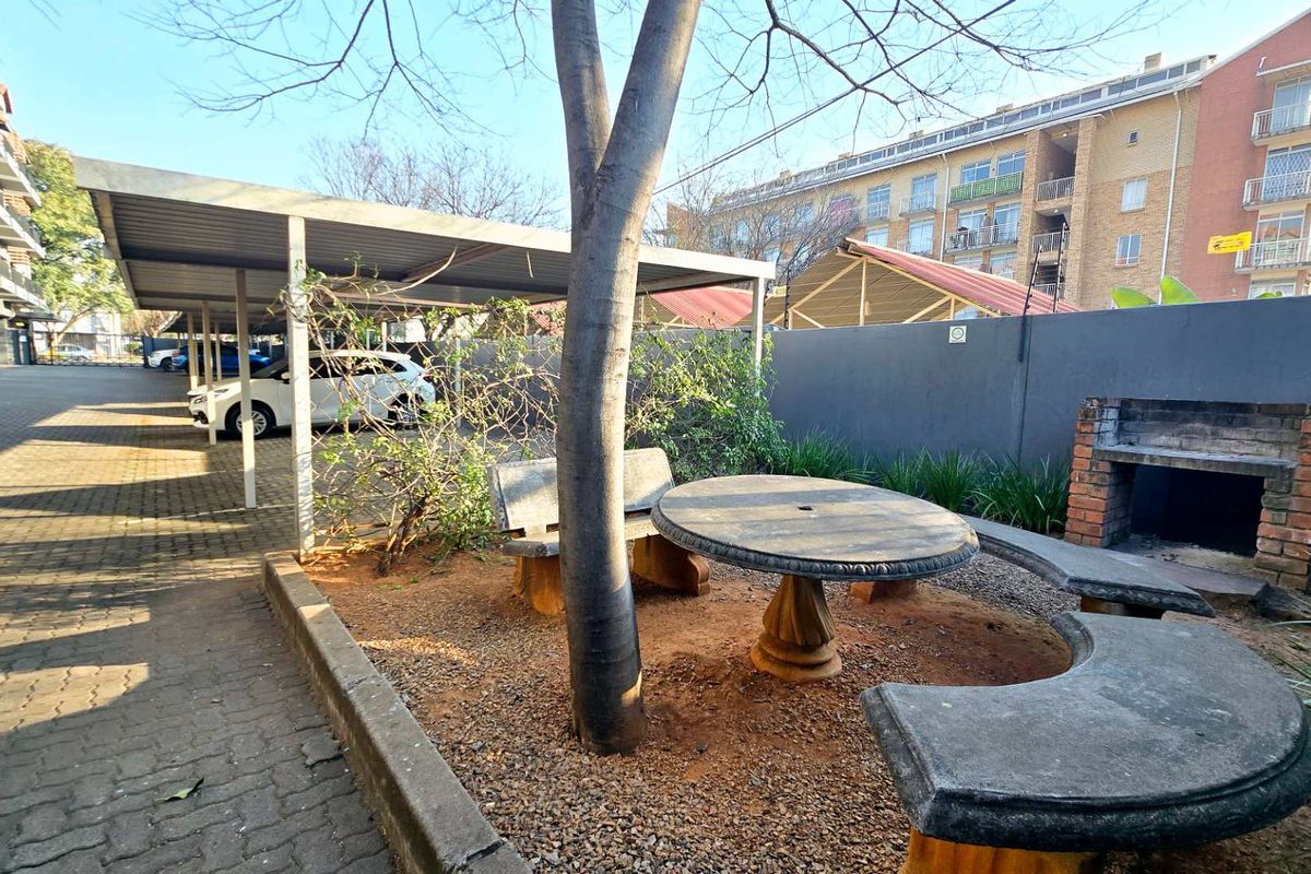 Outdoor communal area featuring a built-in brick braai, stone seating, and covered parking bays within the apartment complex grounds.