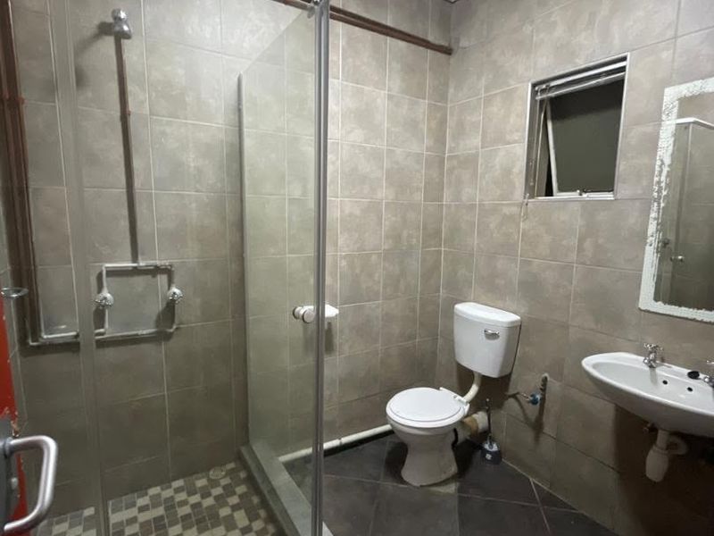 A functional bathroom featuring a glass shower enclosure, wall-mounted basin, and toilet, finished with neutral wall and floor tiling.