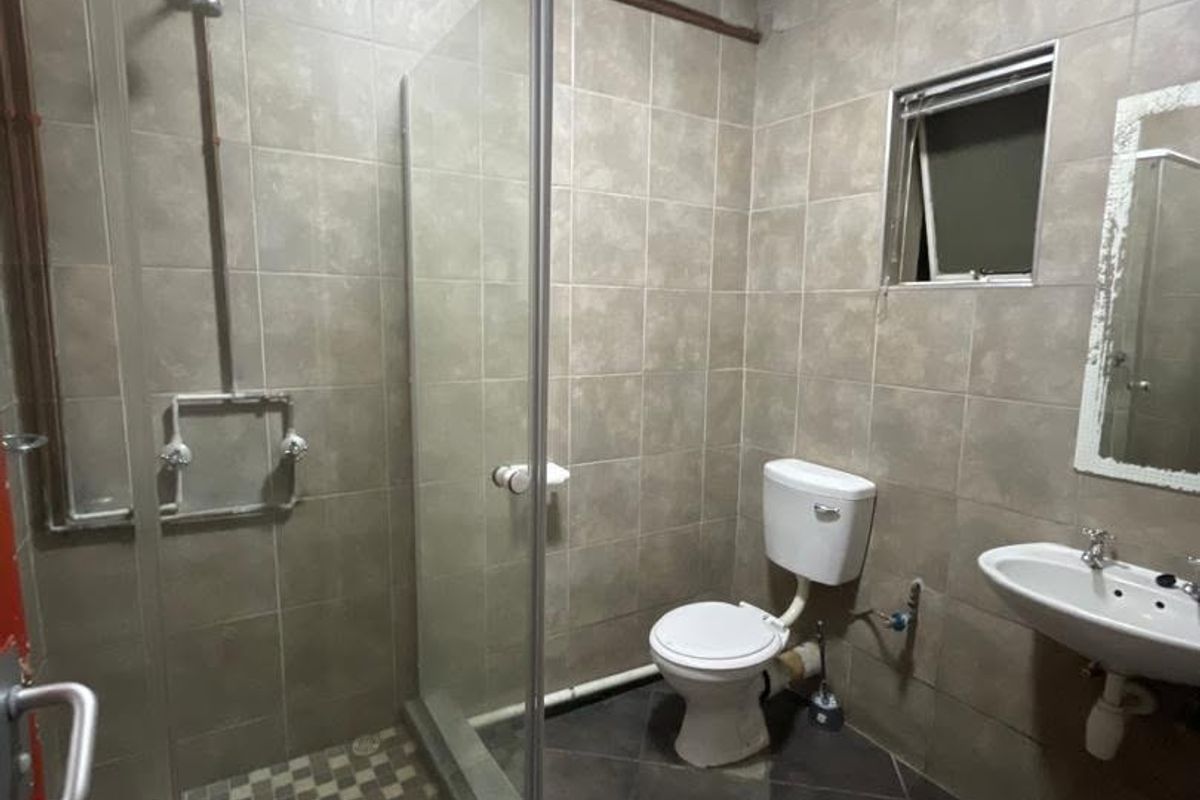 A functional bathroom featuring a glass shower enclosure, wall-mounted basin, and toilet, finished with neutral wall and floor tiling.