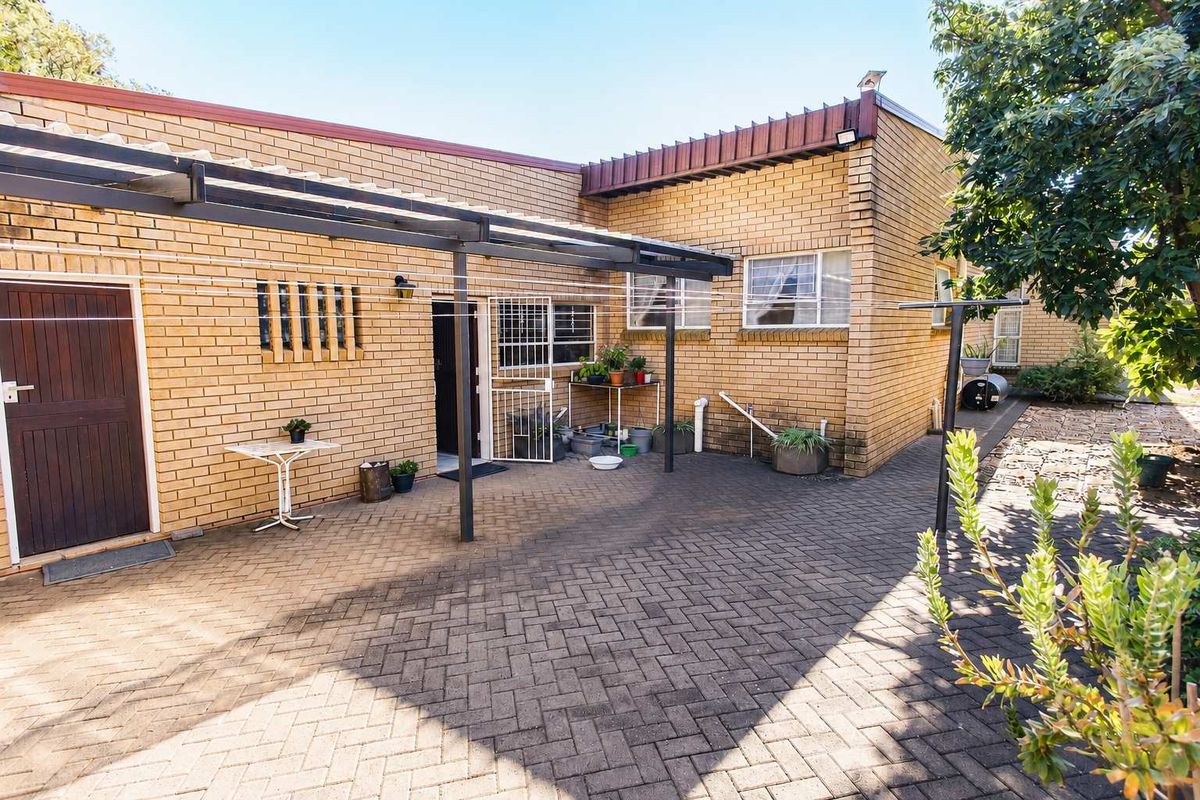 A paved rear courtyard featuring a metal pergola structure, brick exterior walls, and access to the home via a security gate.