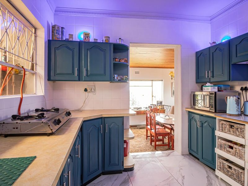 A functional kitchen featuring blue built-in cabinetry, tiled splashbacks, a gas hob, and tiled flooring, with an open doorway leading to the dining area.