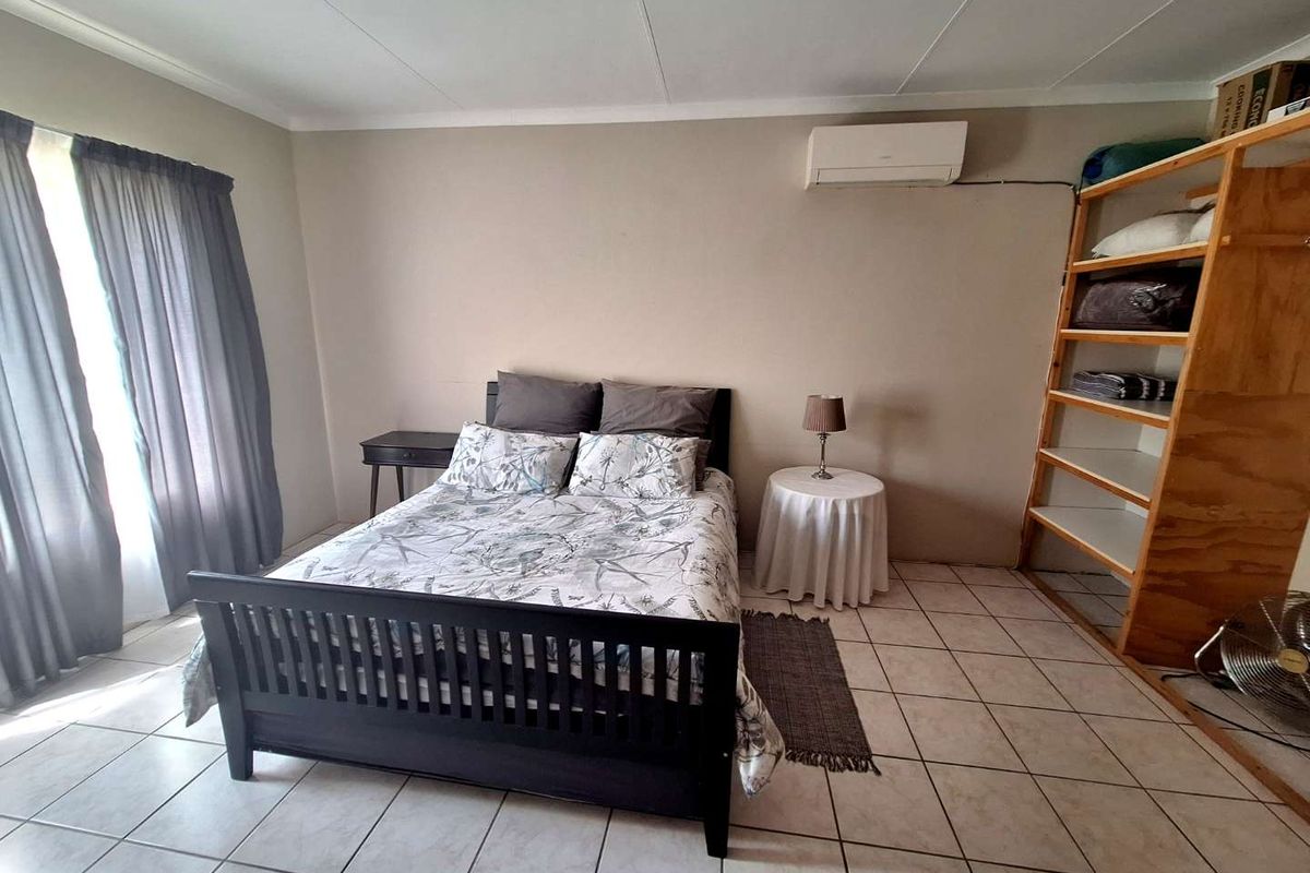 A functional bedroom featuring tiled flooring, a wall-mounted air conditioning unit, and large windows with curtains.