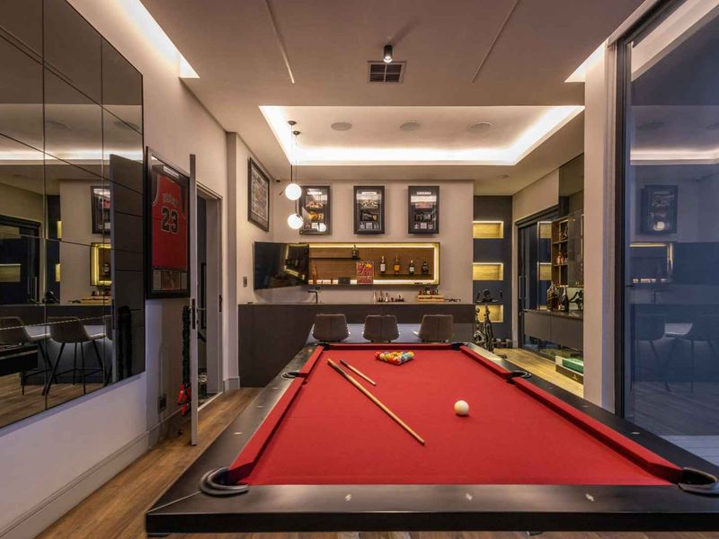 A modern, high-end entertainment room featuring a built-in bar, recessed ceiling lighting, mirrored wall accents, and seamless indoor-outdoor flow through sliding glass doors.