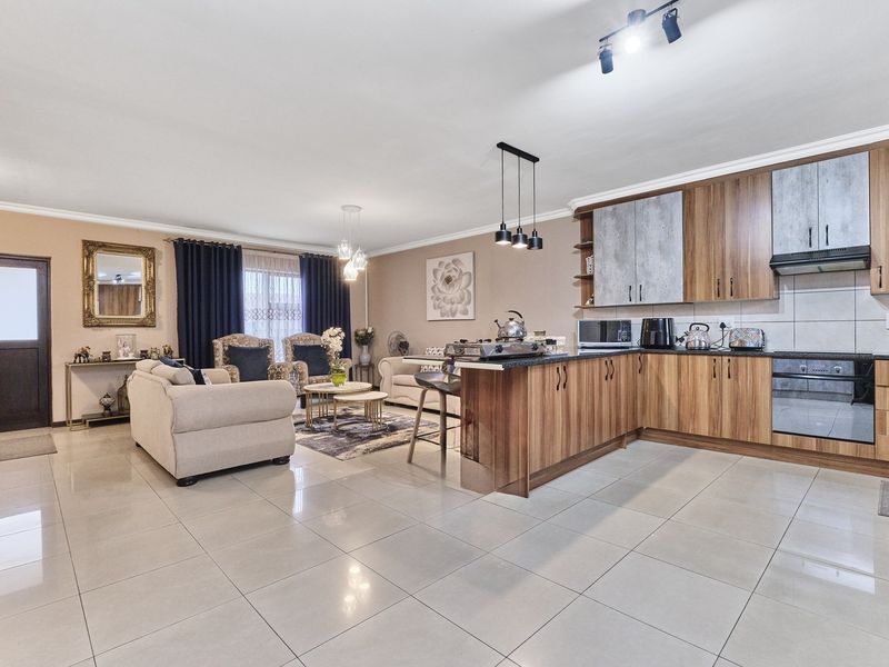 Spacious open-plan living area featuring a modern kitchen with wood-finish cabinetry, integrated appliances, and large format floor tiles throughout.