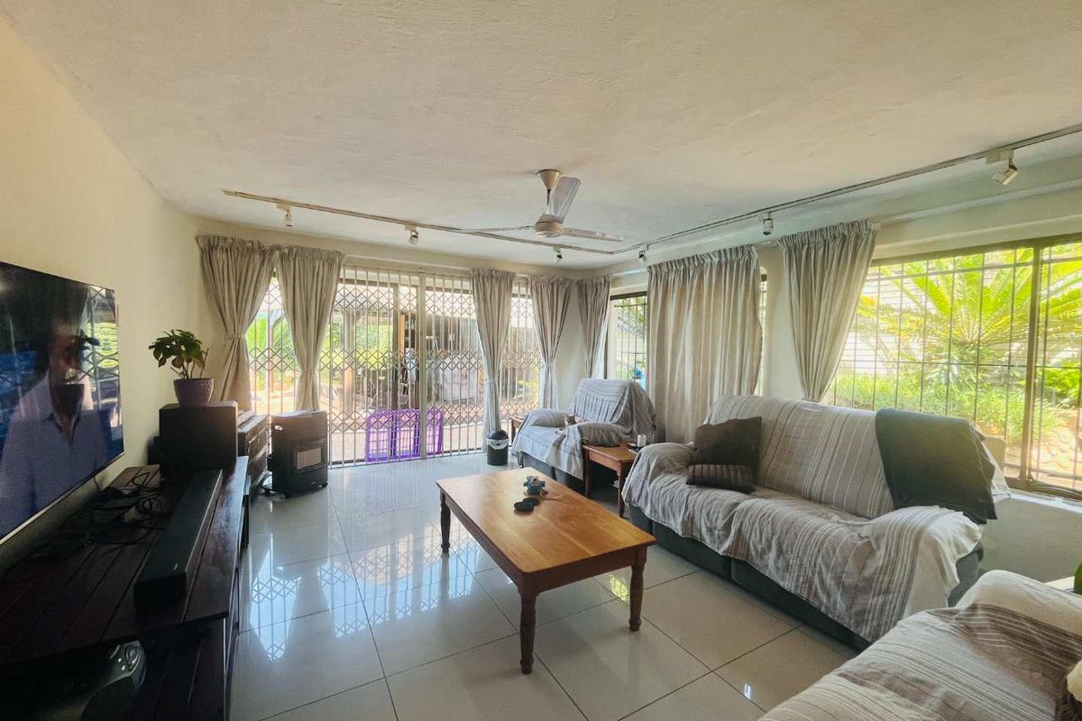 Spacious living room featuring large windows, tiled flooring, and a ceiling fan, providing a bright and comfortable area for relaxation.