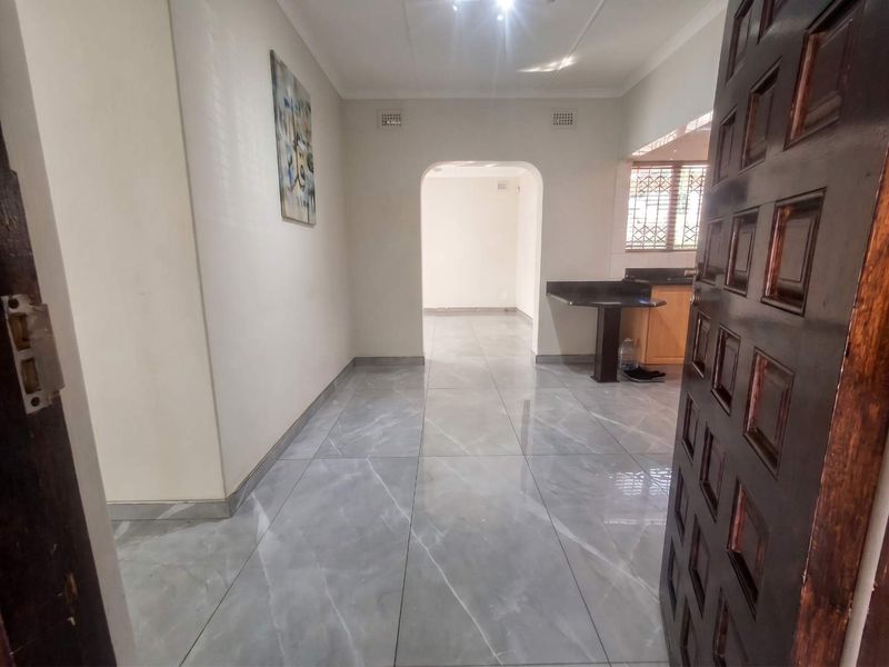 An inviting entrance hall featuring modern grey marble-look floor tiles, leading through an archway into an open-plan living and kitchen area.