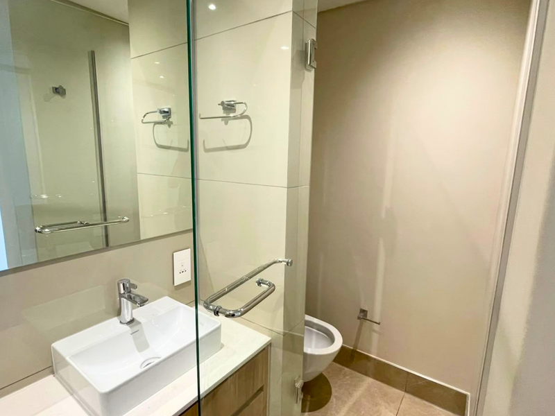 Modern bathroom featuring a sleek vanity with countertop basin, glass shower screen, and neutral wall tiling.