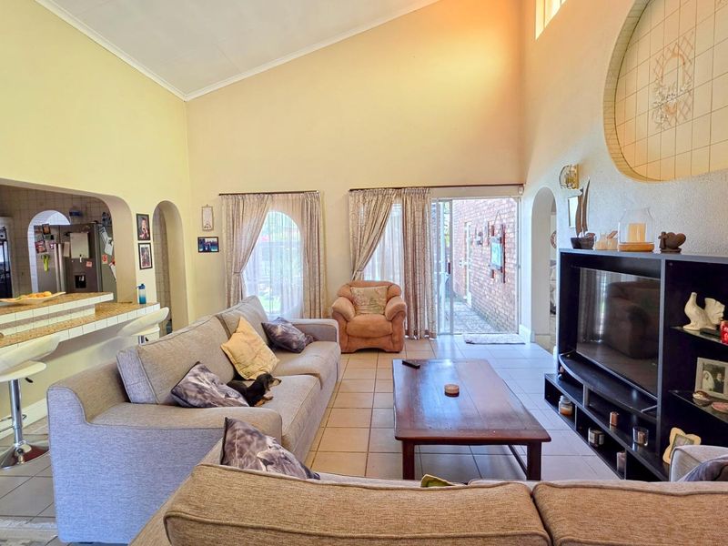 Spacious open-plan living area featuring a vaulted ceiling, tiled floors, and a breakfast bar connecting to the kitchen, with direct access to the patio.