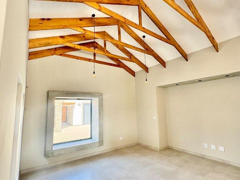 Spacious living area featuring high vaulted ceilings with exposed timber trusses, tiled flooring, and a unique concrete-framed window.