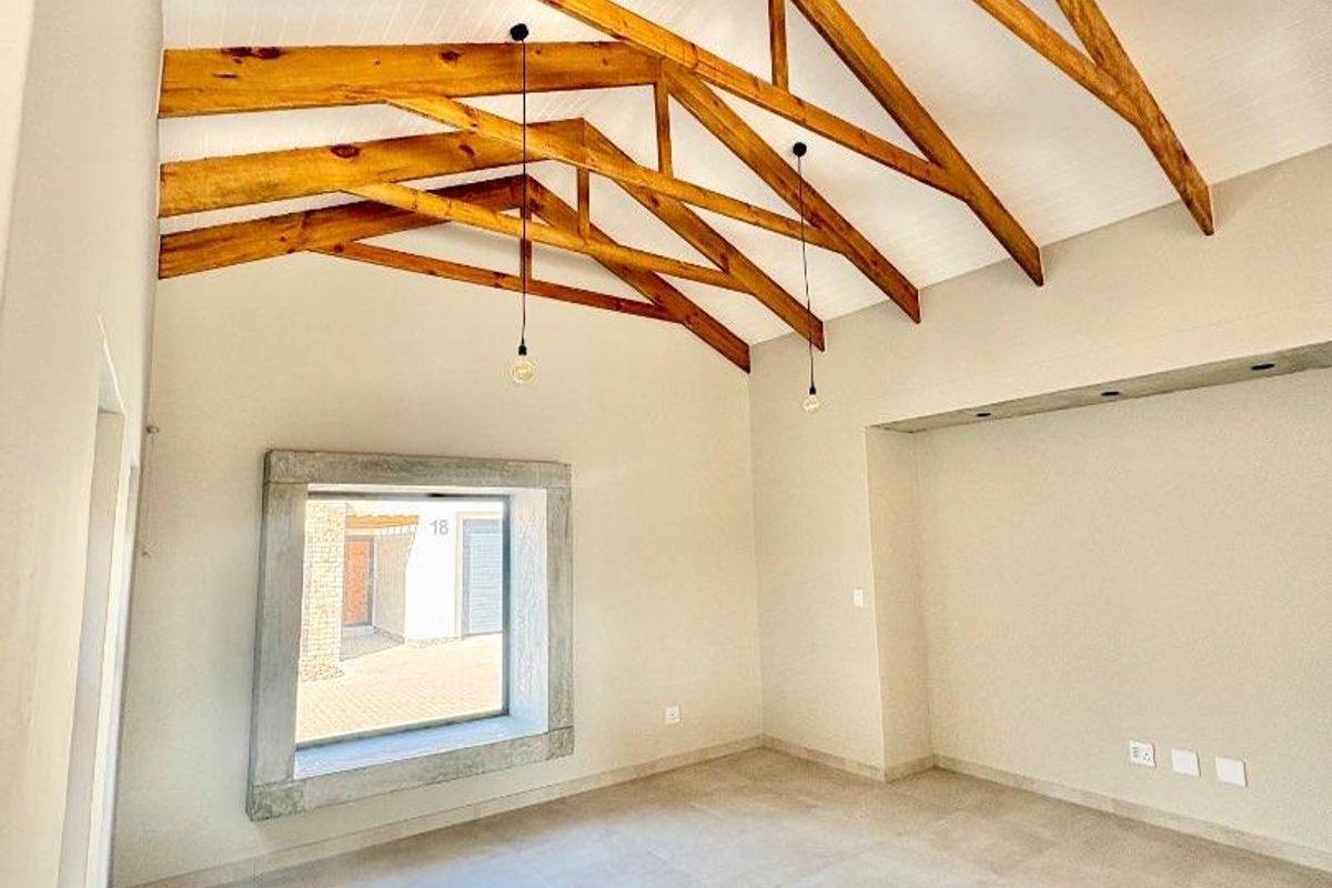Spacious living area featuring high vaulted ceilings with exposed timber trusses, tiled flooring, and a unique concrete-framed window.