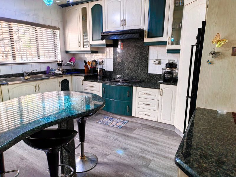 A functional kitchen featuring granite countertops, ample cabinetry, a built-in hob with extractor fan, and a central island with breakfast bar seating.