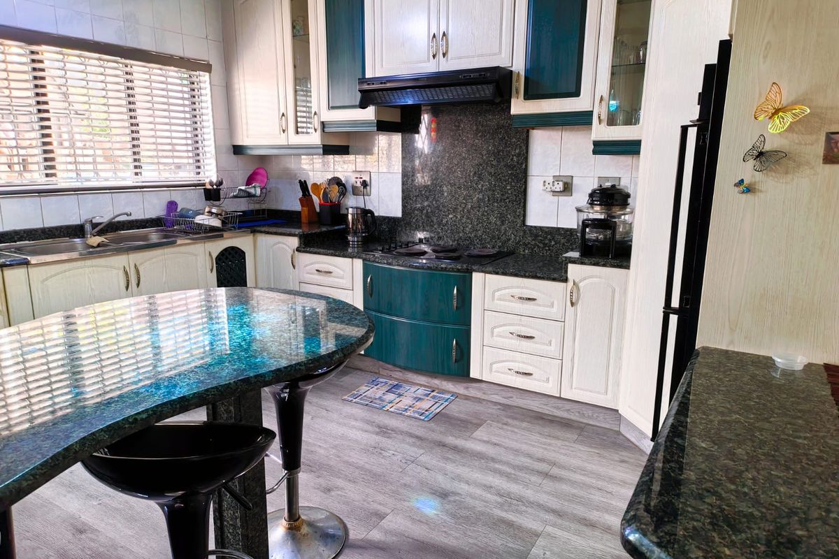 A functional kitchen featuring granite countertops, ample cabinetry, a built-in hob with extractor fan, and a central island with breakfast bar seating.