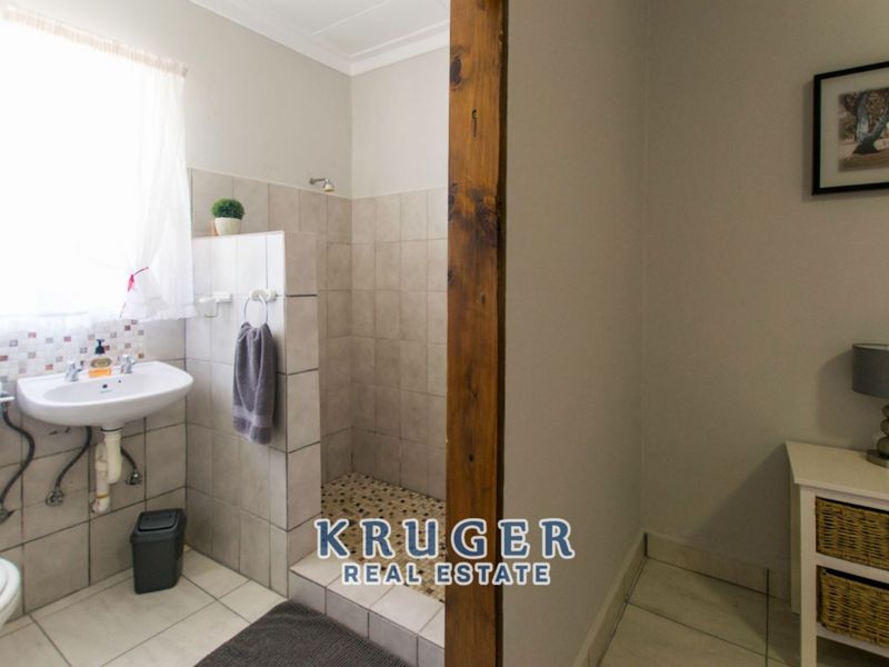 A functional bathroom featuring a walk-in shower with tiled flooring, a pedestal basin, and a toilet, finished with neutral wall tiles.