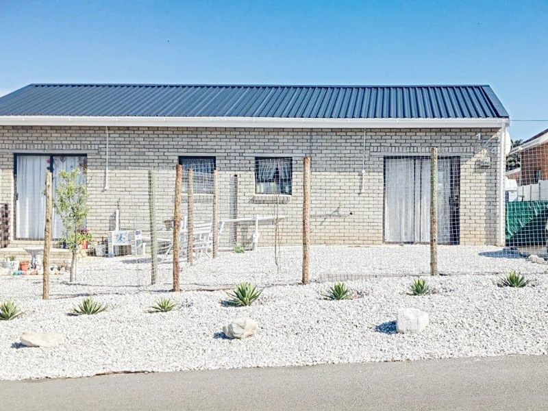 A neat cottage exterior featuring a face brick facade, corrugated metal roof, and low-maintenance gravel landscaping with sliding door access.