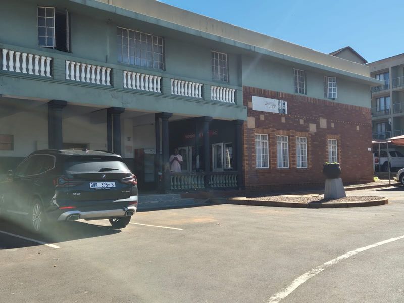 Front exterior view of the apartment building featuring a brick and painted facade with a covered entrance and paved parking area.