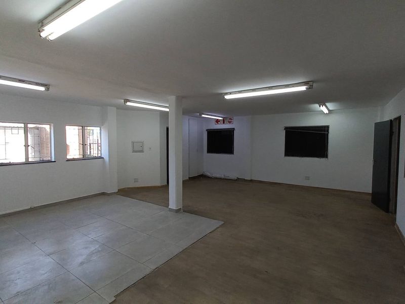 Spacious open-plan industrial office or utility space featuring fluorescent lighting, tiled and vinyl flooring, and multiple windows providing natural light.