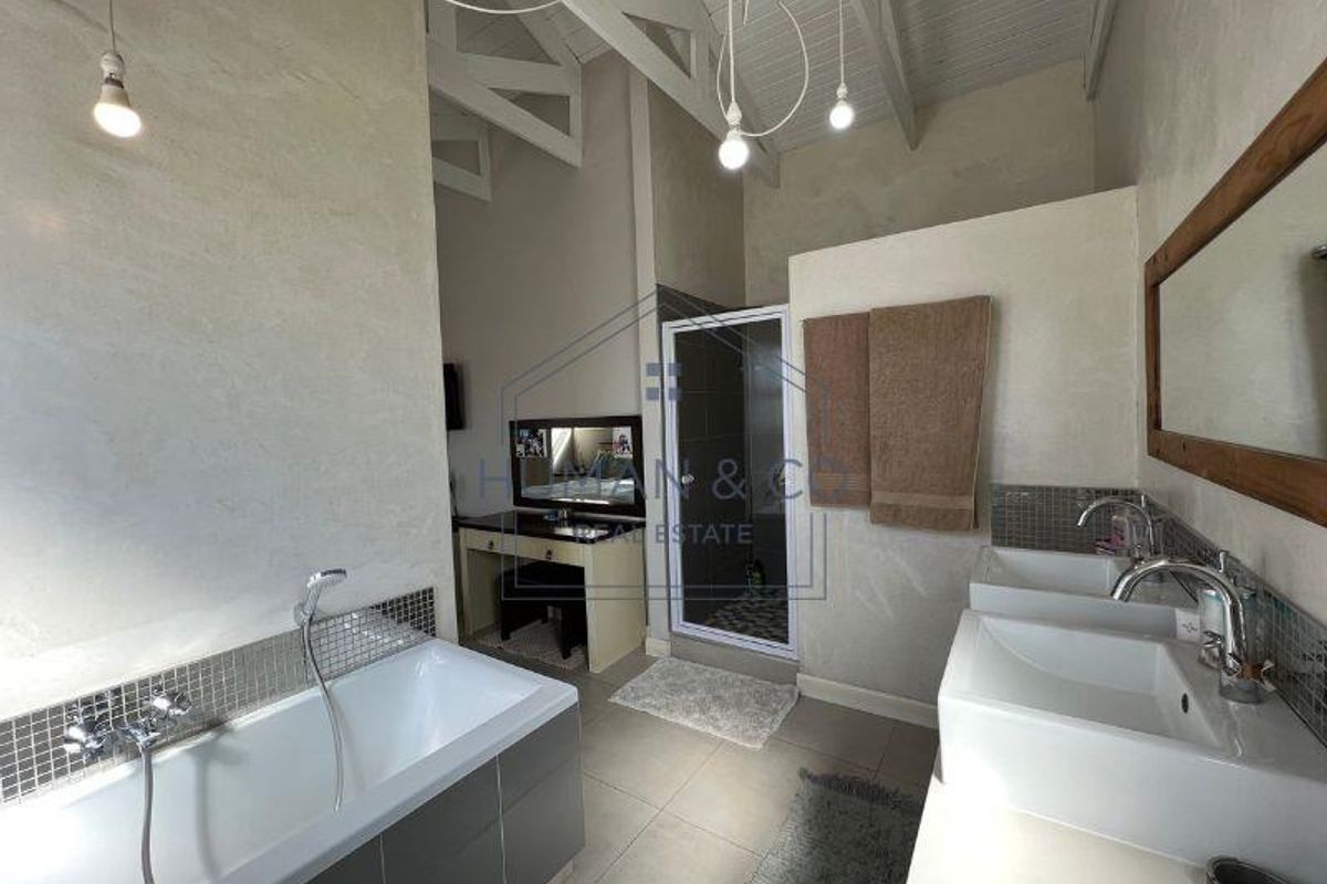 Spacious bathroom featuring a double vanity, a modern bathtub with handheld shower, and a separate glass-enclosed shower stall under a high vaulted ceiling.