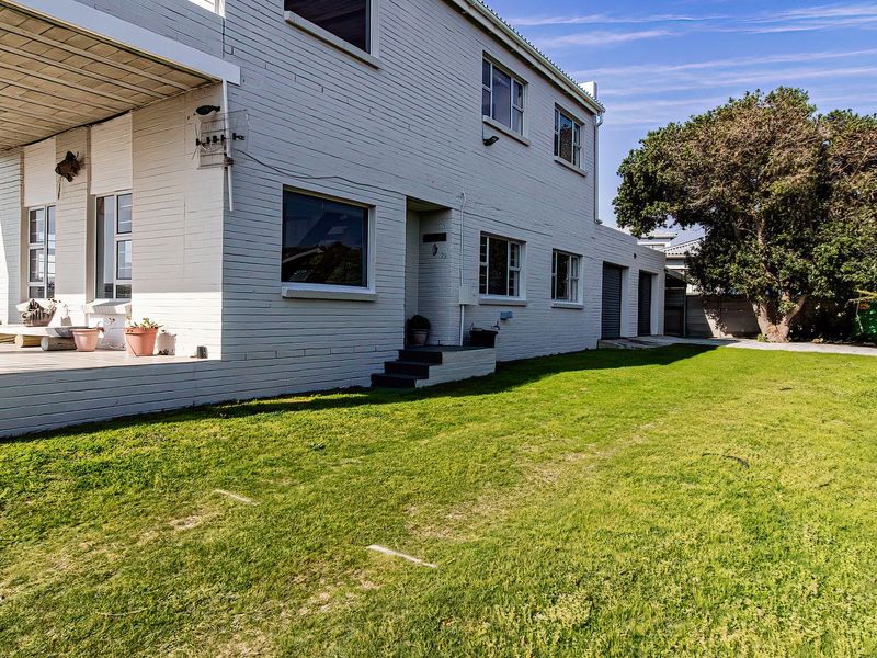 Rear view of a two-story brick house featuring a covered patio area, a spacious lawn, and integrated garage access.
