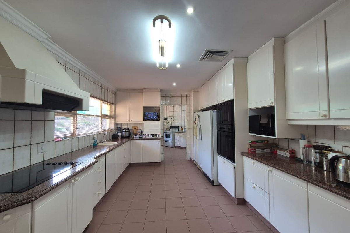 Spacious kitchen featuring granite countertops, built-in appliances, and ample cabinetry, with a connected scullery area visible in the background.