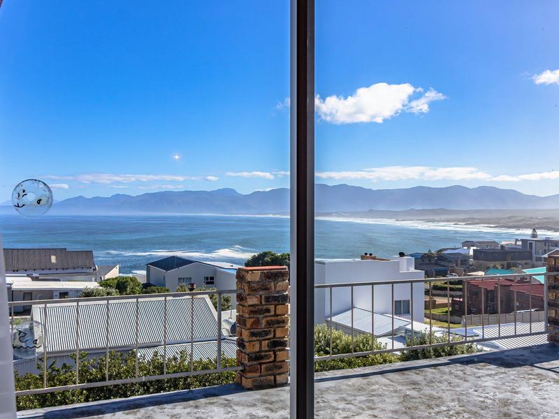 A scenic elevated view of the coastline and mountains captured from a balcony with brick and metal railing details.