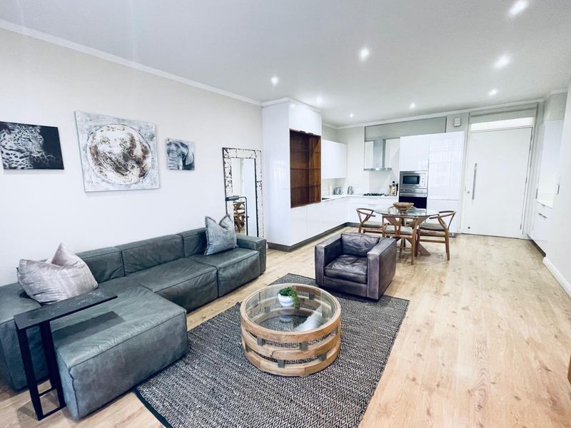 Modern open-plan living area featuring light laminate flooring, recessed lighting, and a sleek, contemporary kitchen with integrated appliances.