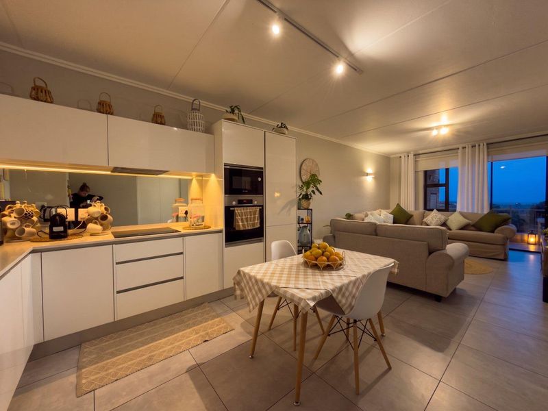 Modern open-plan kitchen and living area featuring sleek white cabinetry, integrated appliances, mirrored splashback, and large sliding doors leading to an outdoor space.