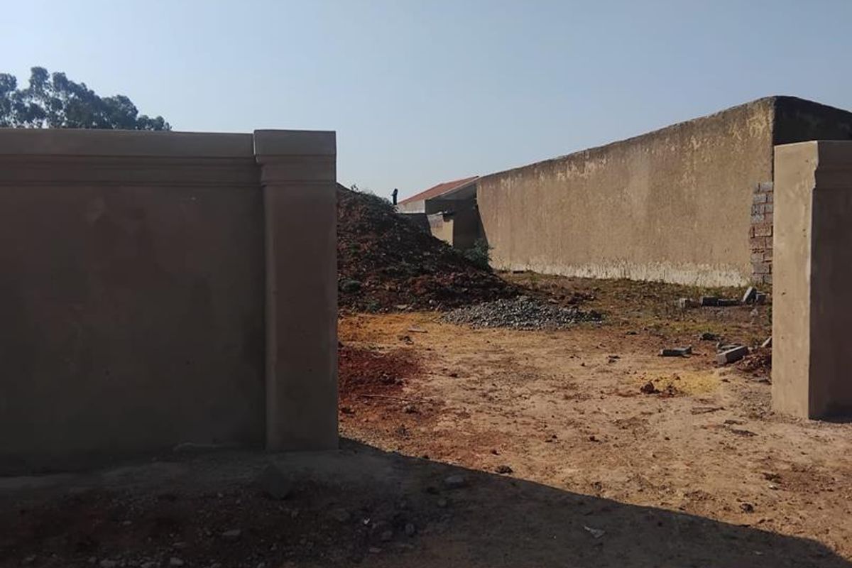 A view of a vacant residential plot featuring perimeter walls and masonry pillars, currently in an unfinished state with loose construction debris on site.