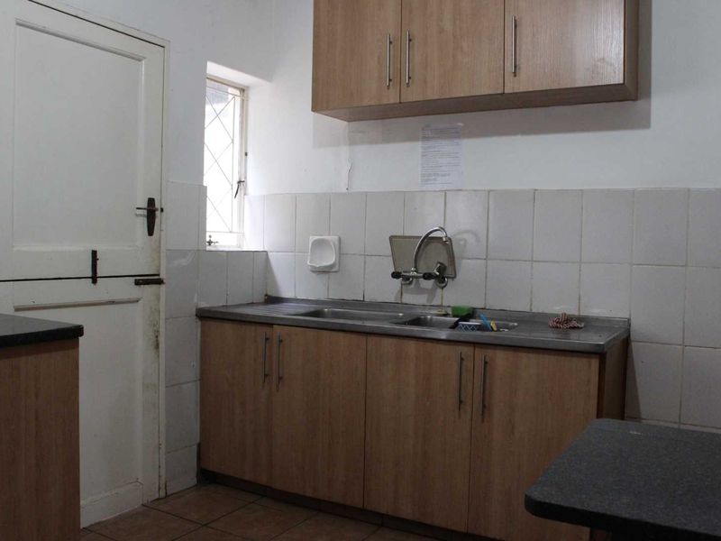 A functional scullery area featuring laminate cabinetry, a stainless steel sink, tiled splashbacks, and tiled flooring.