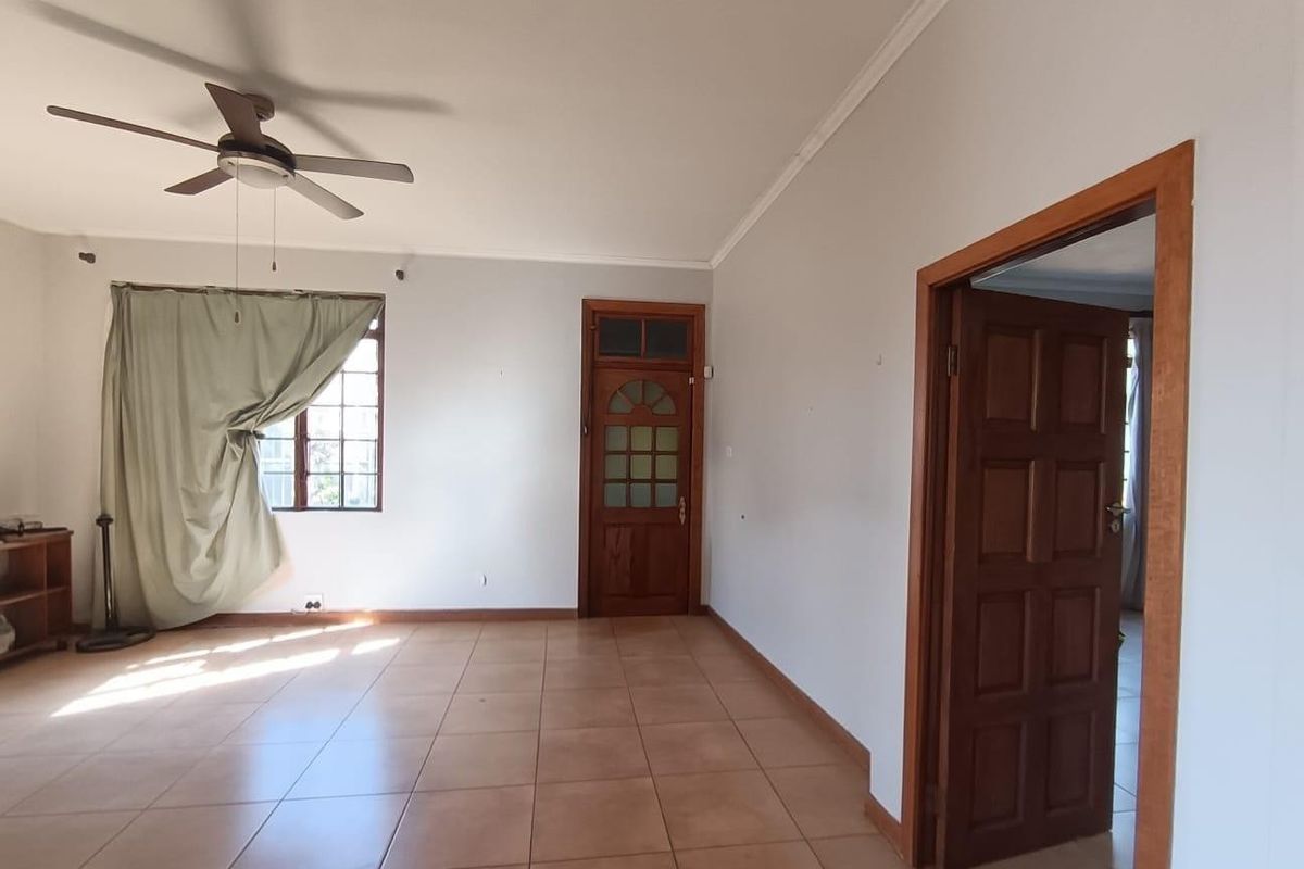 An empty living room featuring tiled flooring, a ceiling fan, and traditional wooden doors, offering a blank canvas for interior design.