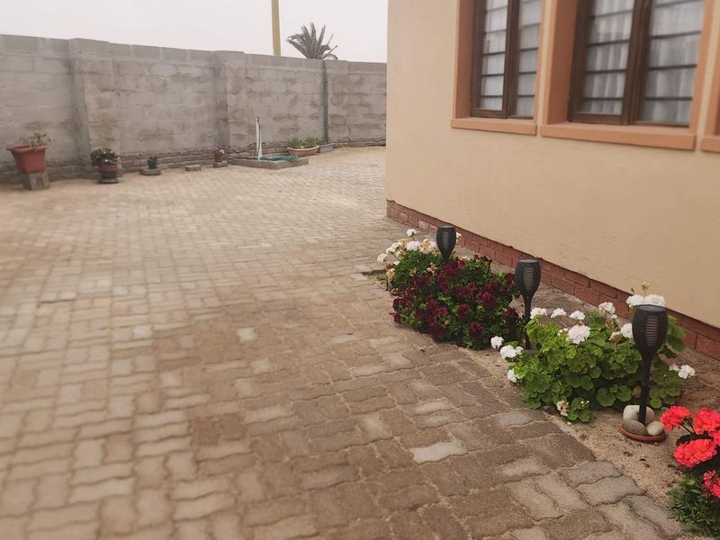 A rear exterior view of the property featuring paved ground surfaces and a concrete block boundary wall.