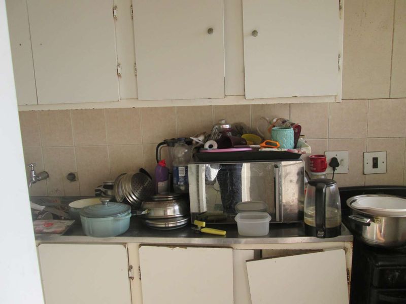 A dated kitchen area featuring built-in cabinetry, a stainless steel countertop, and tiled backsplash, currently showing significant wear and tear.