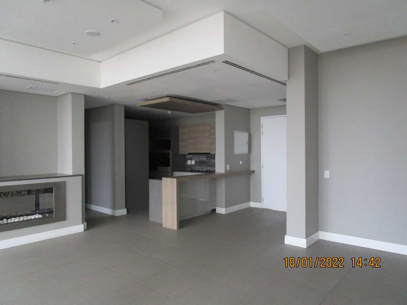 Spacious open-plan living area featuring a modern kitchen with breakfast bar, built-in fireplace, and neutral tiled flooring throughout.