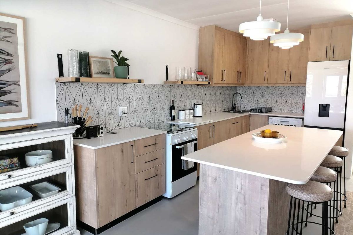 Modern kitchen featuring light wood cabinetry, a central island with breakfast bar seating, geometric patterned backsplash, and integrated appliances.