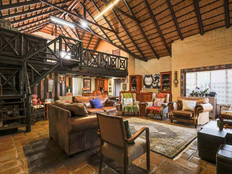 Spacious living area featuring high vaulted ceilings with exposed timber trusses, stone flooring, and a mezzanine level with a timber staircase.