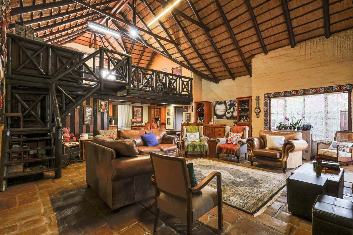 Spacious living area featuring high vaulted ceilings with exposed timber trusses, stone flooring, and a mezzanine level with a timber staircase.