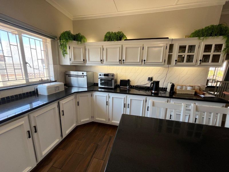 A well-maintained kitchen featuring white cabinetry, dark granite countertops, a tiled backsplash, and wood-look floor tiles with ample natural light.